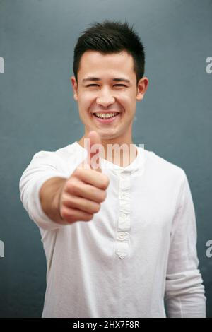 Hope youre having a great weekend. Studio portrait of a handsome young man showing thumbs up against a grey background. Stock Photo