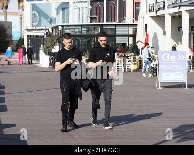 ASHKELON, ISRAEL - MARCH 04, 2022: young people looking into smartphones while walking on city street. Stock Photo