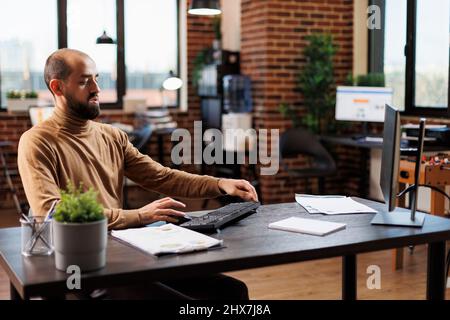Company entrepreneur developing financial solutions while sitting at desk in office and using work computer. Management department team leader analyzing investment ideas. Stock Photo