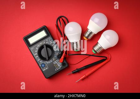 Multimeter and energy saving bulbs on red background Stock Photo