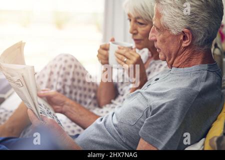 The newspaper gives them a start for the day. Shot of a senior couple lying in bed. Stock Photo