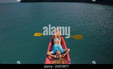 Pretty slim woman in elegant swimsuit lies in pink plastic kayak drifting on azure ocean at exotic resort upper view. Traveling to tropical countries. Stock Photo