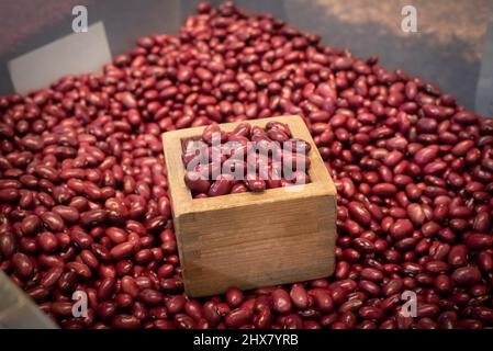 Red azuki beans in a wooden cube masu measuring container at an Asian supermarket and wet market. Stock Photo