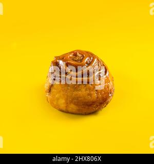 Cinnamon roll with caramel topping on yellow background Stock Photo