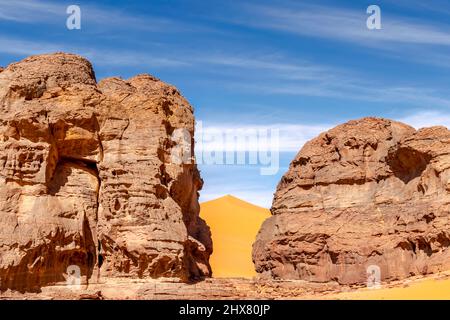 Big sand dune between two stone mountains in the Sahara Desert of Tadrart Rouge, Djanet, Algeria. Far unrecognezible tourists on the peak. Blue sky. Stock Photo