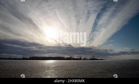 Sunset shining through heavy chemtrail. Seascape at sunset in winter Stock Photo