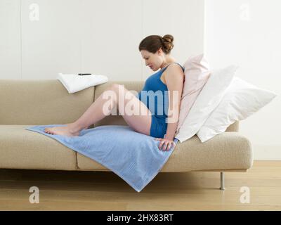 Pregnant woman sitting on sofa covered with towel during home-birth labour Stock Photo