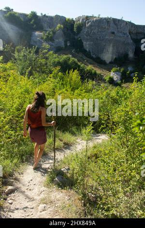 Girl walks along mountain path. Walk in wild. Tourist descends from mountains. Rest in summer. Woman with stick in her hands walks unknown road among Stock Photo
