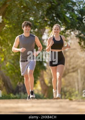 Young couple doing sports running on a park path and smiling Stock Photo