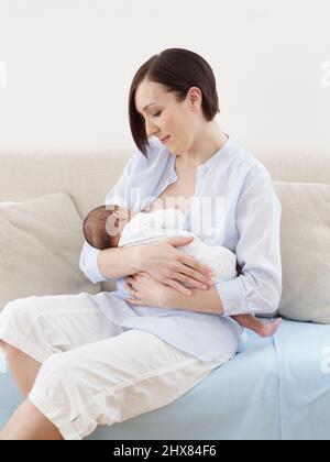 Woman sitting breastfeeding baby girl, 6 weeks Stock Photo