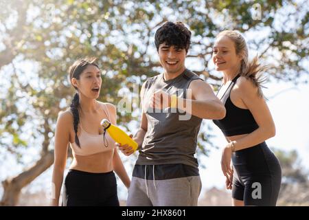 Three young people doing sports look at the smart watch and laugh in the park Stock Photo