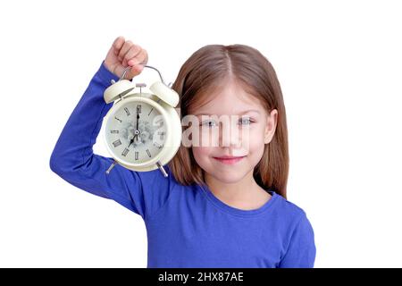 Child holding alarm with 7 o'clock on clock face, isolated on white background looking at camera waist up caucasian little girl of 5 years in blue Stock Photo