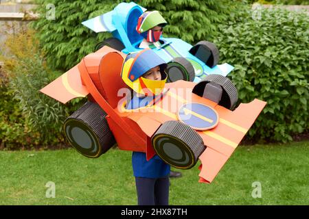 Children wearing Cardboard racing car models/costume, playing in garden Stock Photo
