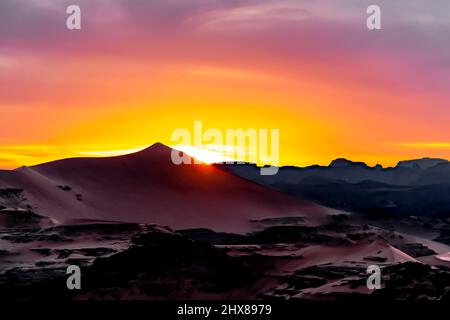 Colorful sunset behind a huge sand dune landscape. Aerial view from the peak of a sand dune of Rocky Mountains and cloudy multi-coloured sky.