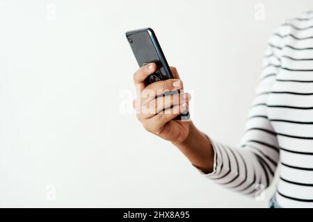 Friends are never far away with your smartphone. Cropped shot of a woman using a smartphone against a white studio background. Stock Photo