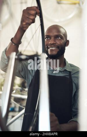 Making sure its aligned. Shot of a handsome young man standing alone in his shop and repairing a bicycle wheel. Stock Photo