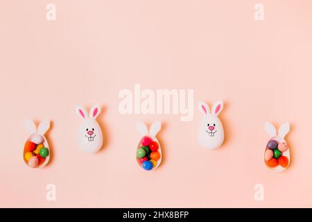 Top view festive Easter beige peach color background with funny bunny eggs containers filled with candy chocolate eggs. Bunny rabbit symbol. Easter eg Stock Photo