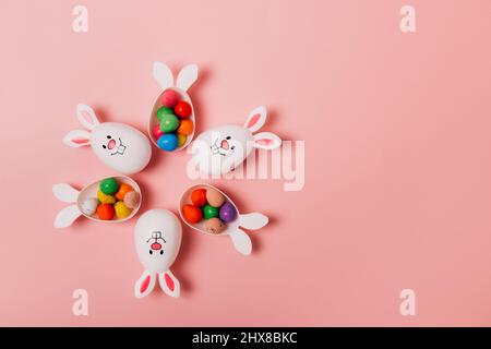 Top view Easter pink background with flower shape made of funny eggs containers with bunny ears filled with candy chocolate eggs. Bunny rabbit symbol. Stock Photo