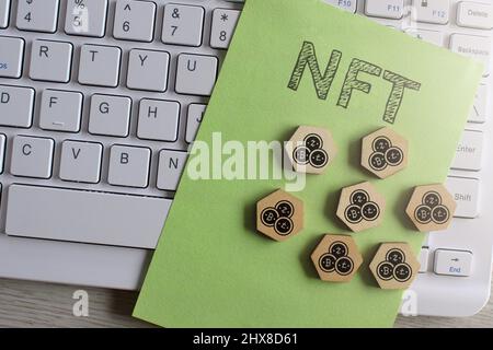 Top view image of keyboard, paper with text NFT and wooden hexagon with cryptocurrency icon. Stock Photo