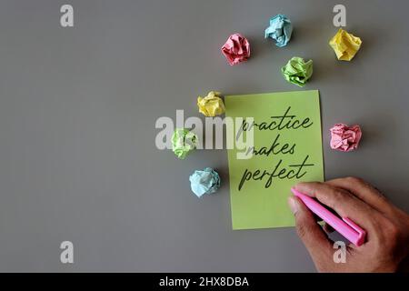 Top view image of hand holding pen, crumpled paper and green paper with text PRACTICE MAKES PERFECT. Stock Photo