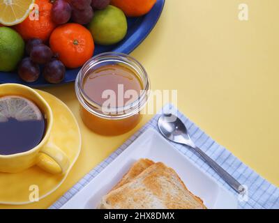 honey with toast, tea with lemon and a plate of fruit stand on a yellow tablecloth Stock Photo