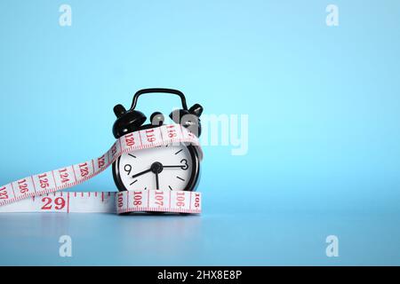 Alarm clock and measuring tape on blue background with copy space. Stock Photo