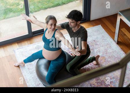 Blonde pregnant woman practicing yoga with her partner at home Stock Photo