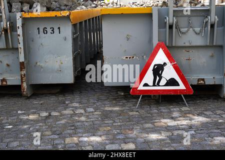 Containers with cobble stones and other construction material. In front of them there is a traffic sign work on the road. Stock Photo