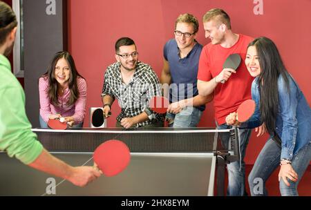 Group of happy young friends playing ping pong table tennis - Fun moment in game room of traveler youth hostel - Concept of vintage sport and genuine Stock Photo