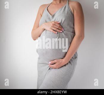 pregnant woman in gray dress on white background studio shot Stock Photo