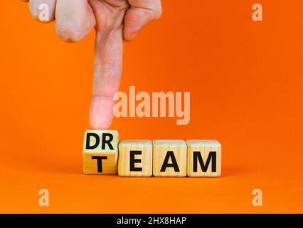 Dream team dreamteam symbol. Businessman turns wooden cubes and changes the word Dream to Team. Beautiful orange table orange background. Business and Stock Photo
