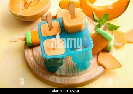 Board with tasty popsicles and melon pieces on yellow background Stock Photo