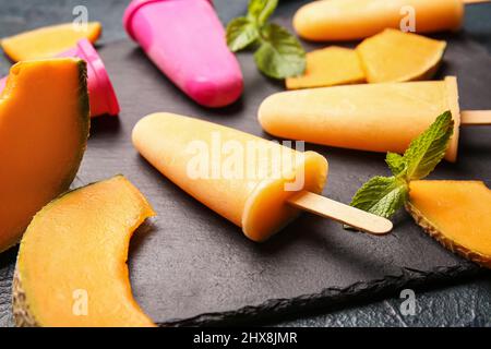 Board with tasty popsicles and melon pieces on dark background Stock Photo