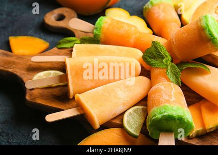 Board with tasty popsicles and melon pieces on dark background Stock Photo