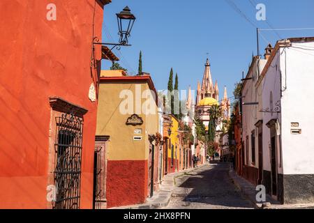 Mexico, Guanajuato,San Miguel de Allende, a side street in the city with houses and shops leading into town with  Parroquia de San Miguel Arcángel Stock Photo