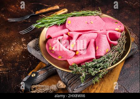 Slices of Salami with pistachios nuts in steel plate with thyme and rosemary. Dark background. Top view Stock Photo