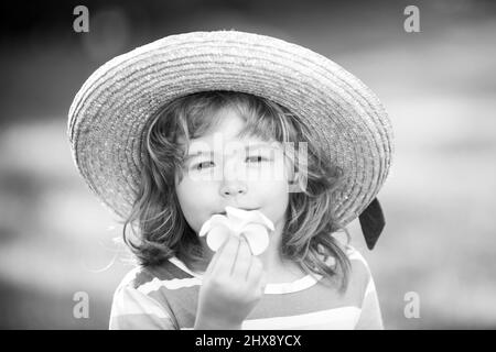 Portrait of a cute child boy in straw hat smelling plumeria flower. Close up caucasian kids face. Closeup head of funny kid. Stock Photo