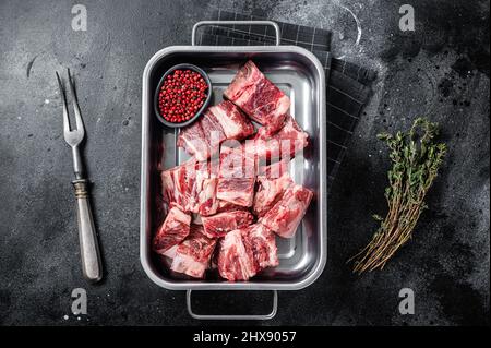 Raw sliced diced beef meat in steel tray with herbs. Black background. Top view Stock Photo