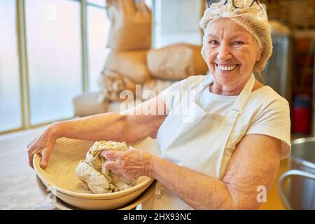 Happy elderly woman baker kneading dough in a bowl in preparation for baking Stock Photo