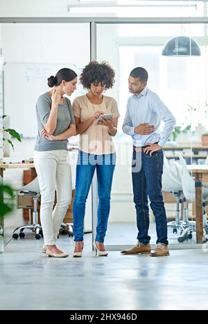 Three great minds think alike. Shot of a group of office colleagues having a discussion over a digital tablet. Stock Photo