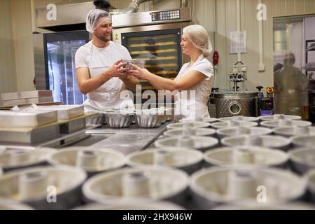 Two bakers bake a lot of Gugelhupf cakes together in a large bakery Stock Photo