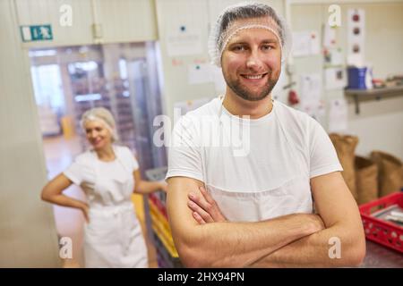 Young man as a proud baker's apprentice with his arms crossed in a bakery's bakery Stock Photo