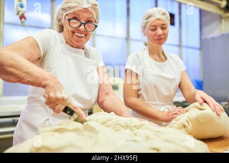 Two female bakers cutting and kneading the dough in preparation for baking bread Stock Photo