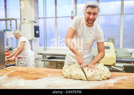 Baker trainee cuts dough with a knife while kneading bread dough Stock Photo