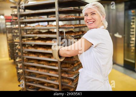 Cheerful young woman as a baker's apprentice pushes ready-baked croissants in the bakery Stock Photo