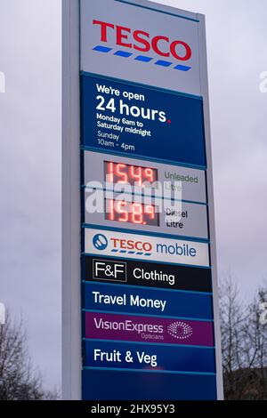 Wigan, UK: March 10, 2022: Large illuminated sign at entrance to Tesco supermarket car park showing company logo, opening hours and price per litre of Stock Photo