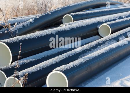 Plastic water pipes. Black PVC tubes plastic pipes stacked on white snow background. Water supply repair. Heating houses in winter. House Stock Photo