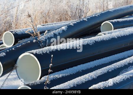 Plastic water pipes. Black PVC tubes plastic pipes stacked on white snow background. Water supply repair. Heating houses in winter. House Stock Photo