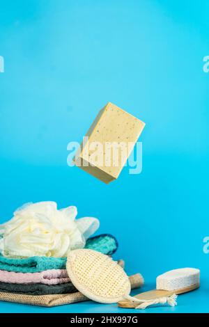 Herbal soap floating with folded towels, brushes, scrub stone on blue background. Stock Photo