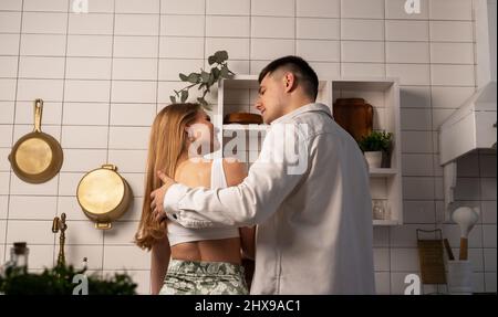 Back view of young happy couple cooking at home. Young handsome man hugging girlfriend or wife. Beautiful woman smiling and tenderly looking at husband or boyfriend. High quality photo Stock Photo